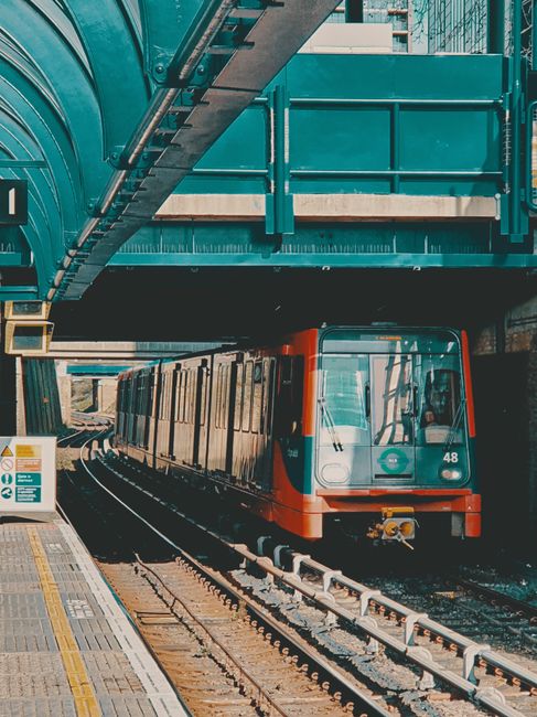 The image depicts a modern underground train approaching a station platform, with the train's front facing forward. The train has a sleek, streamlined design with a predominantly white exterior accent